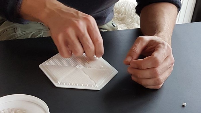 En person laver perler på en sort overflate.