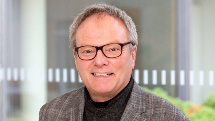 Professioneller Mann im Anzug und mit Brille, der drinnen in der Nähe von Glastüren lächelt.