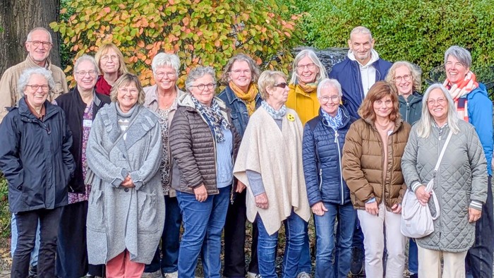 Eine gemischte Gruppe lächelnder Menschen vor einer grünen Hecke