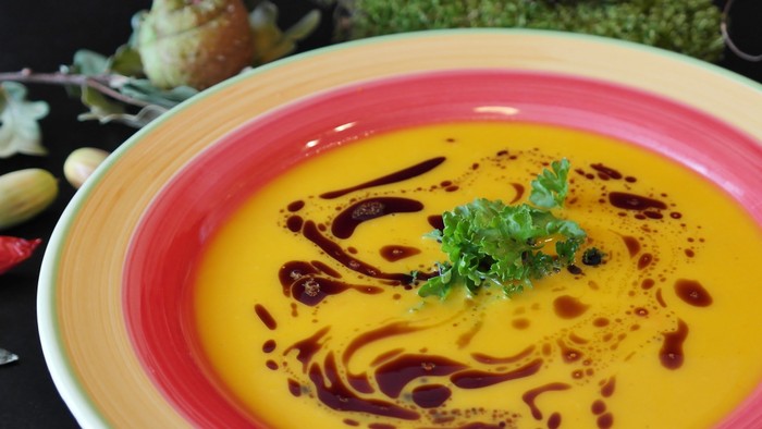 Warme, cremige Orangen-Suppe, beträufelt mit Balsamico-Reduktion und garniert mit Kräutern in einer bunten Schüssel.