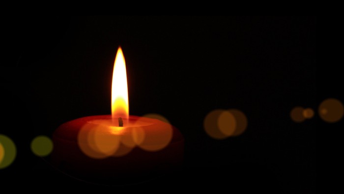 Eine brennende Kerze vor einem dunklen Hintergrund mit Lichtflecken.