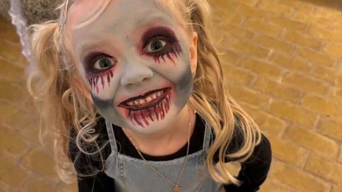 Et lille pige med horror-makeup og grå overall.