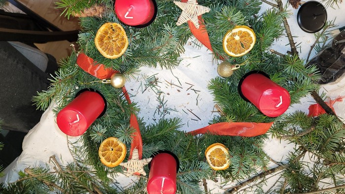 Handgefertigter Weihnachtskranz, geschmückt mit Kerzen, Orangen, Karotten und festlichen Dekorationen auf Kiefernzweigen.