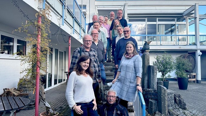 Gruppe von Personen, die draußen vor einem modernen Wohngebäude mit Treppen und Topfpflanzen posieren.