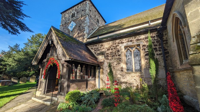 Historic stone church adorned with festive greenery and red flowers, featuring a quaint porch entrance.