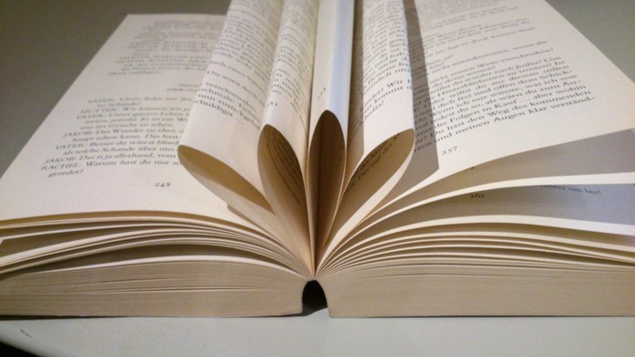 Ein offenes Buch mit papiernen Seiten in Blütenform zwischen seinen Blättern, das auf beiden Seiten Text zeigt.