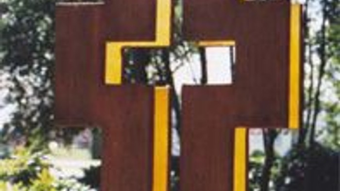Ein großes Holzkreuz mit gelben Streifen in einem Garten.