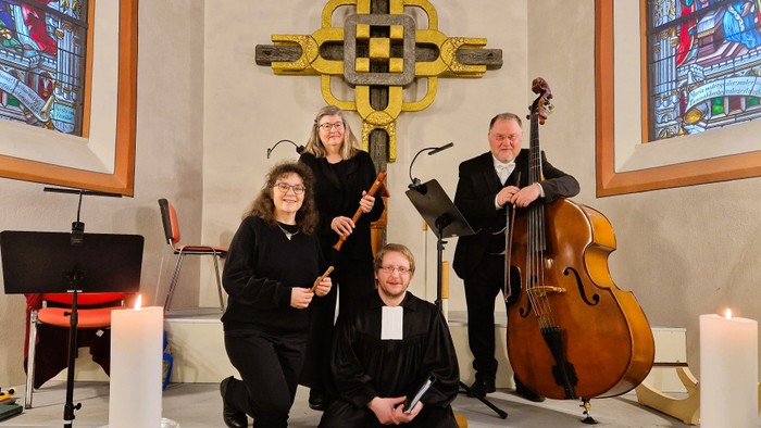 Musiker und Geistliche posieren gemeinsam in einer Kirche mit Musikinstrumenten und bunten Glasfenstern.