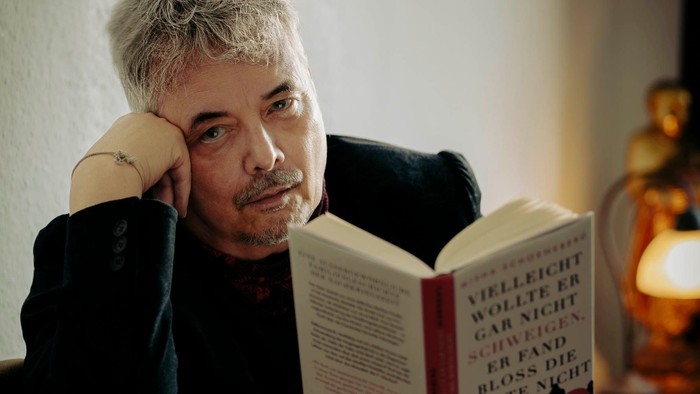 Eine Person mit kurzen Haaren liest ein Buch mit einem deutschen Titel und einem nachdenklichen Gesichtsausdruck.