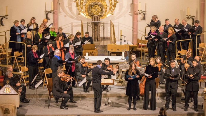 Ein Orchester probt in einer Kirche unter einem großen Kronleuchter