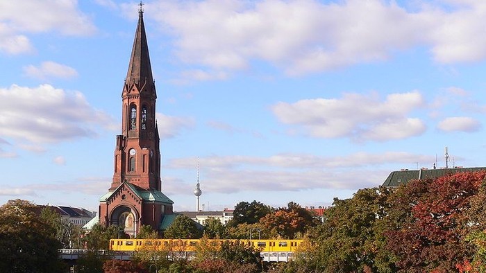 Kirchturm mit spitzem Dach vor Herbstbäumen und blauen Himmel