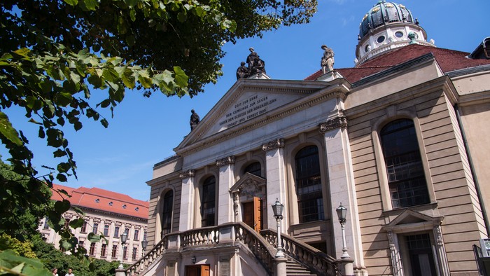 Großes, prächtiges Gebäude mit Treppe und Kuppel, umgeben von Bäumen