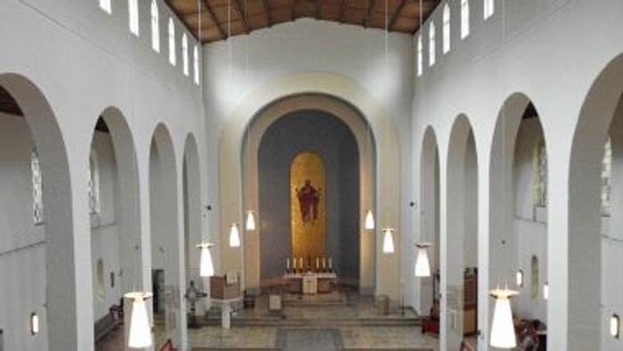Die Kirche hat eine helle, moderne Gestaltung mit einem großen Kreuz an der Wand.