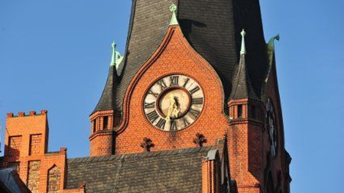 Das Bild zeigt den Turm einer Ziegelkirche mit einem Uhrwerk.