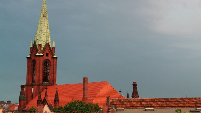 Rote Kirche mit hohem Turm und grünem Dach vor blauem Himmel
