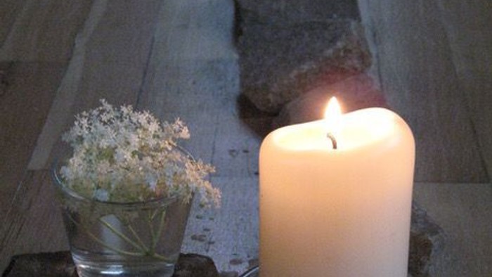 Eine Kerze, Muscheln und eine kleine Vase mit Blumen auf einem Holztisch