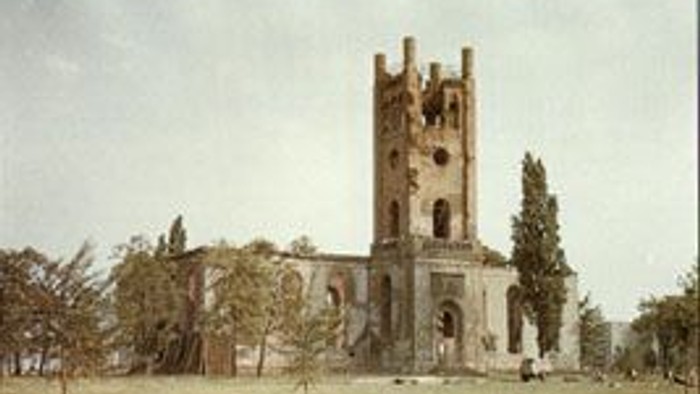 Das Bild zeigt eine alte Kirche mit einem hohen Turm in einem Park.