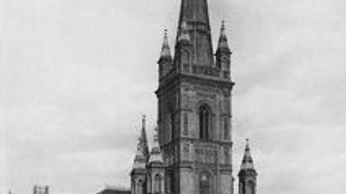 Das Bild zeigt eine große gotische Kirche mit hohem Turm in einer Stadt.