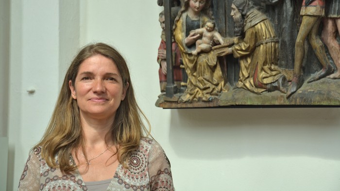 Eine Frau steht vor einer religiösen Holzskulptur.