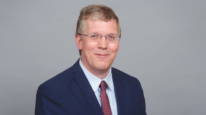 Mann im Anzug mit Krawatte und Brille lächelt.