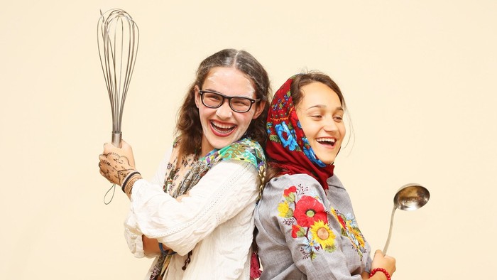 Zwei Mädchen lachen und halten Kochutensilien.