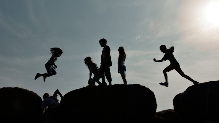 Silhouetten von Kindern springen und spielen auf Felsen unter klarem Himmel