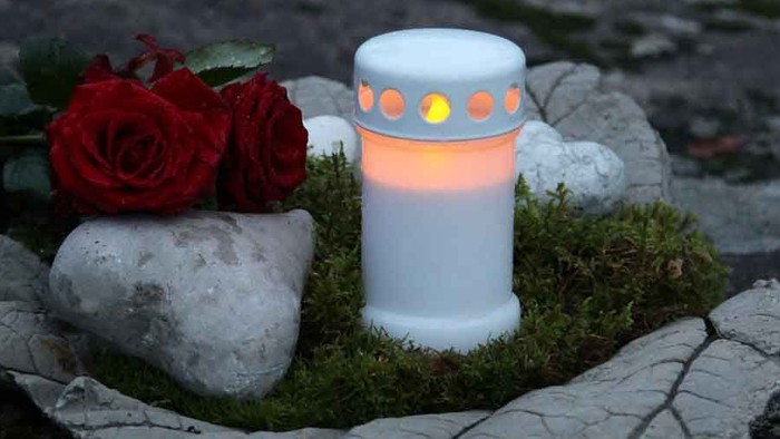 En lysende lysstake med røde roser og sten på en græsplads