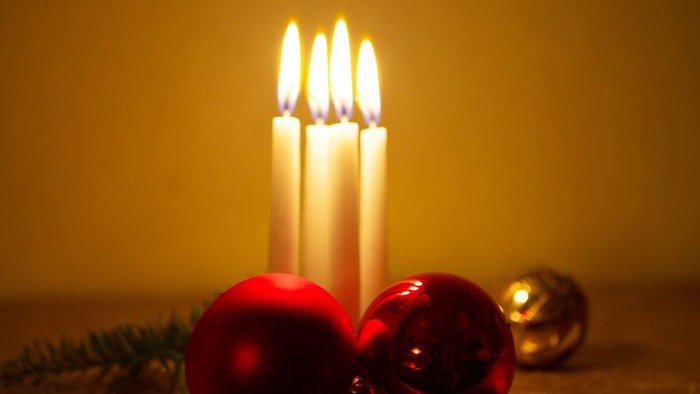 En lyse julelygte med tre lysende lys og to julekugler på bordet