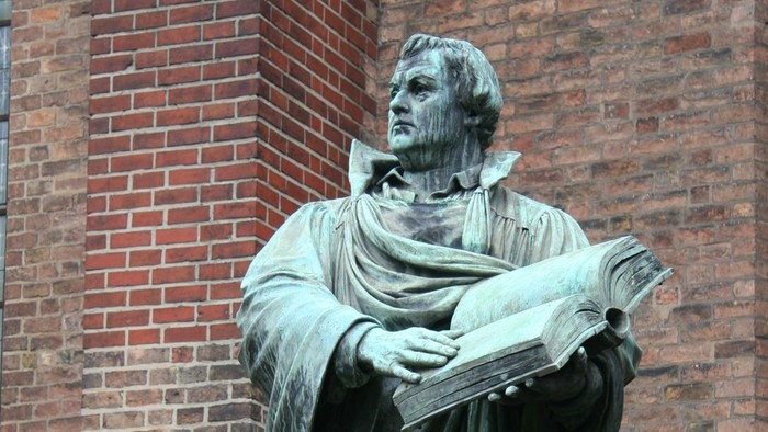 Statue eines Mannes mit Buch vor Ziegelmauer