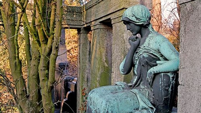 Die Bronzestatue einer Frau sitzt nachdenklich auf einem Sockel.