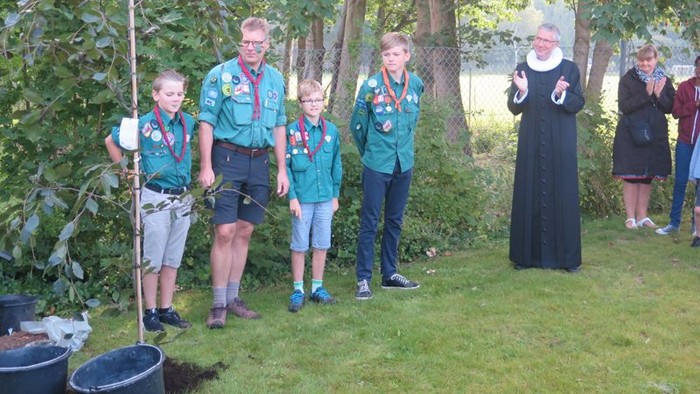 En gruppe spejdere og en nonne står ved et plantetræ.