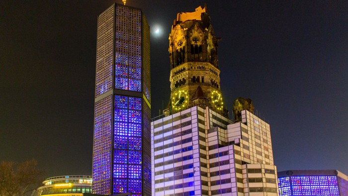 Moderner Wolkenkratzer neben historischem Uhrturm bei Nacht