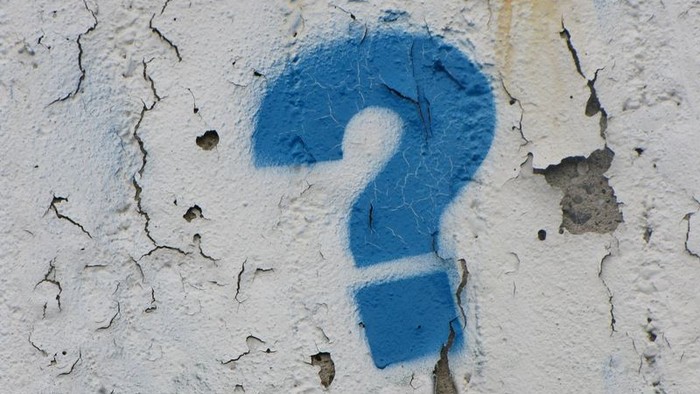 Ein blaues Fragezeichen ist auf einer abblätternden weißen Wand gemalt.