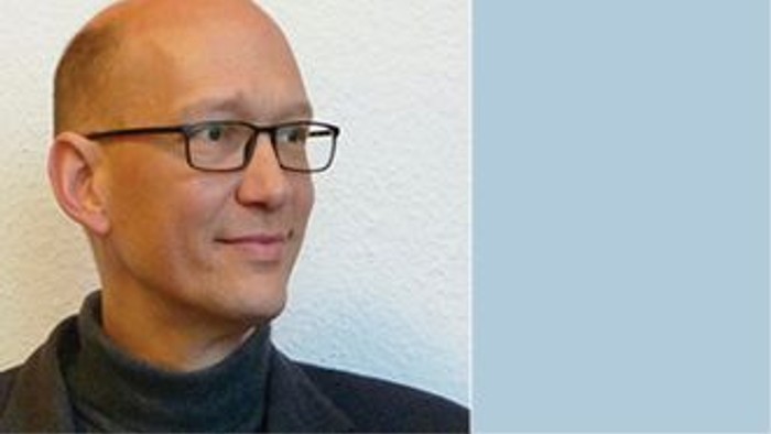 Ein kahlköpfiger Mann mit Brille und schwarzem Rollkragenpullover.