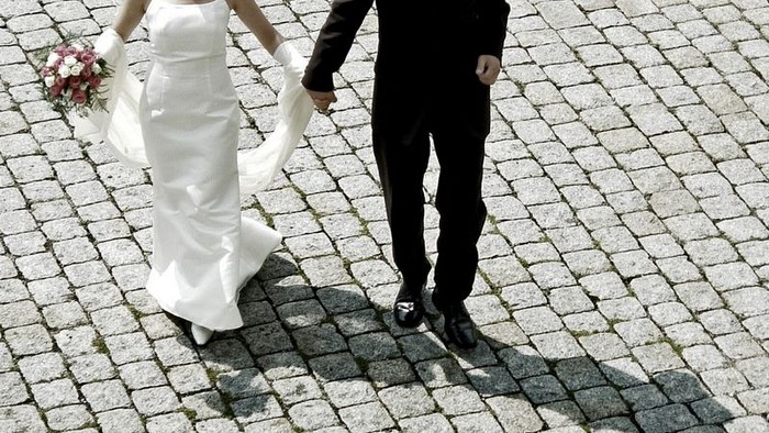 Ein Brautpaar geht Hand in Hand über Kopfsteinpflaster.
