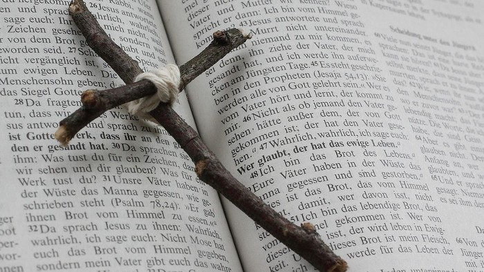 Geöffnetes Buch mit gekreuzten schwarzen Federn, die auf einem deutschen Bibeltext liegen.