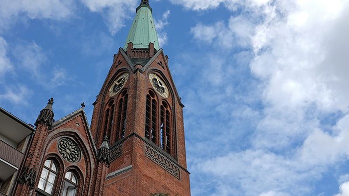 Ein roter Ziegelbau mit hohem Turm und grünem Dach vor blauem Himmel