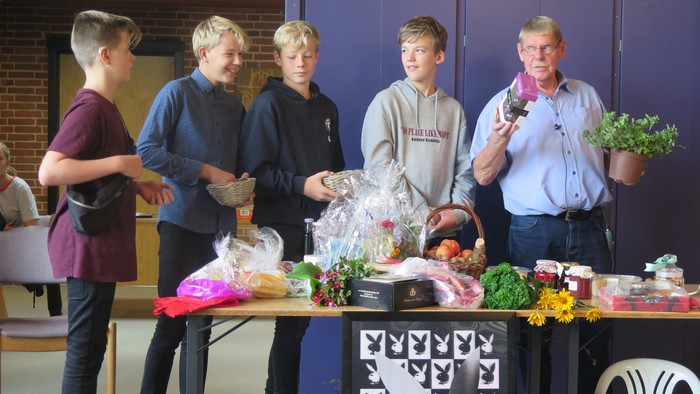 En gruppe drenge står ved en bord med planter og gaver, mens en mand holder en lille plante.