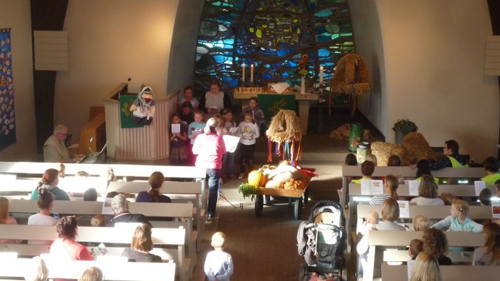In der Kirche versammeln sich Menschen, Kinder spielen vorne.