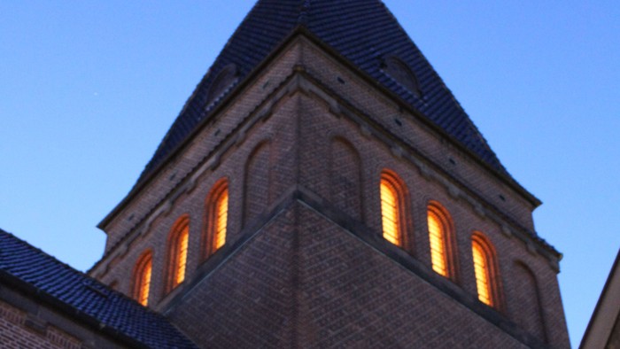 Kirketårn med lysede vinduer mod aftenhimmel