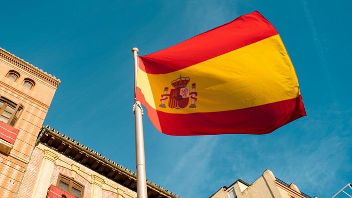 Die spanische Flagge weht vor einem Gebäude am klaren blauen Himmel.