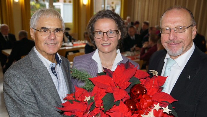 Drei Personen mit Weihnachtsstern posieren in festlichem Raum