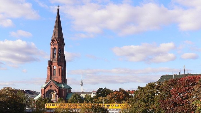 Kirchturm mit spitzem Dach vor Herbstbäumen und blauen Himmel