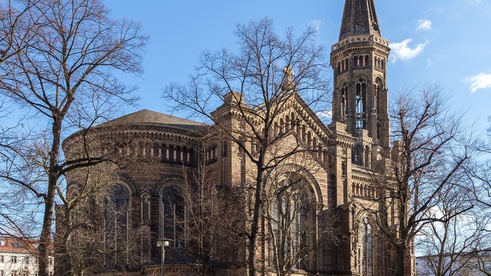 Große Kirche mit hohem Turm und spitzen Dach, umgeben von Bäumen und Autos