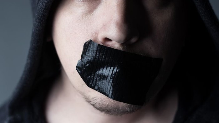 Ein junger Mann mit schwarzem Tape über dem Mund und dunkler Kleidung.