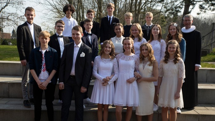 En gruppe ungdomme og piger i festlige klæder og unge mænd i formelle klæder samlet til et billede på trinnene foran et træ.