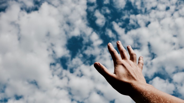 Hand reaching towards cloudy sky
