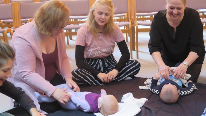 En gruppe kvinder omgiver en baby på en matte i en kirke.