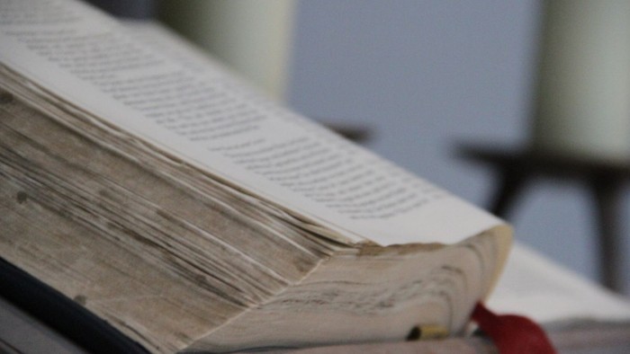 Ein offenes Buch mit einem roten Lesezeichen, das auf einem Stapel anderer Bücher liegt.