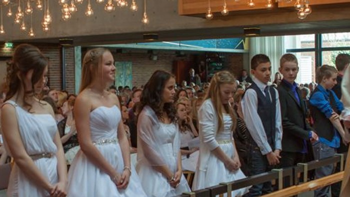 En præst udfører en ceremoni for en gruppe unge piger i hvide kler.